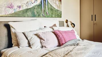 A neatly made bed with a headboard, a bedside table with a lamp, and a large painting above the bed.