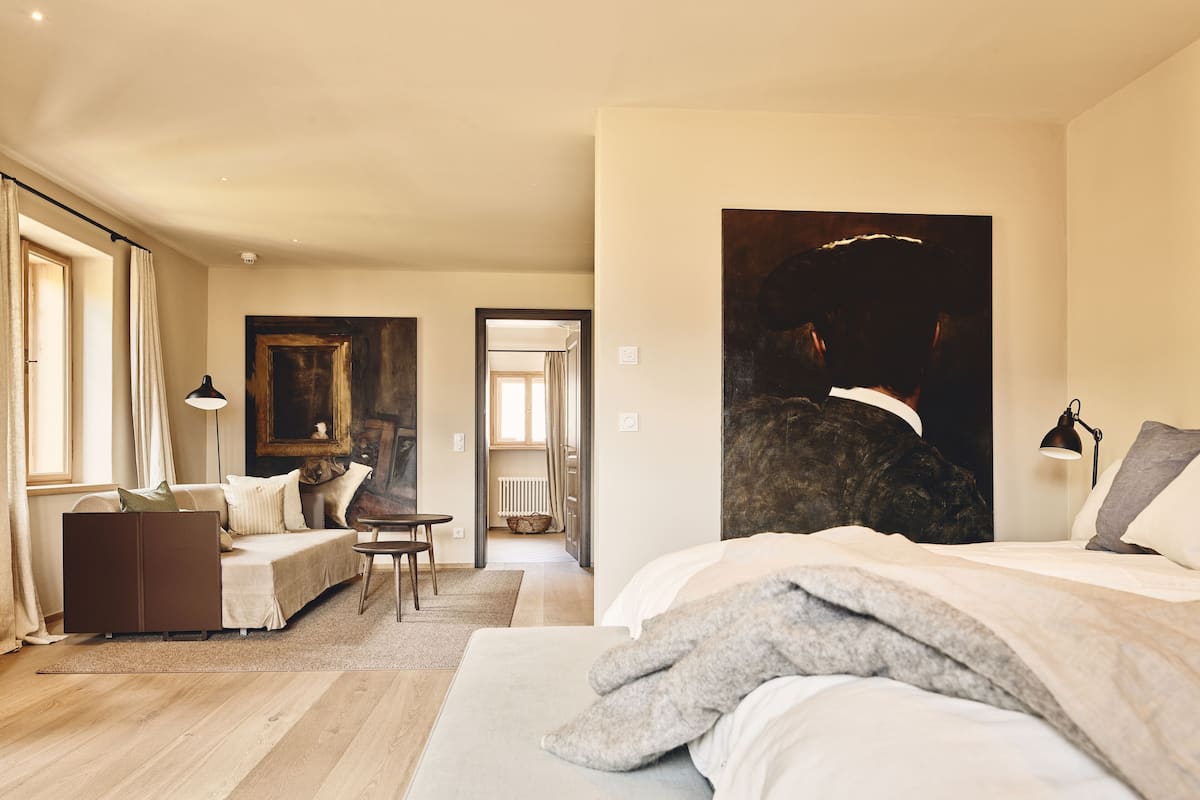 A bedroom with a bed, a desk, a chair, and a painting on the wall.