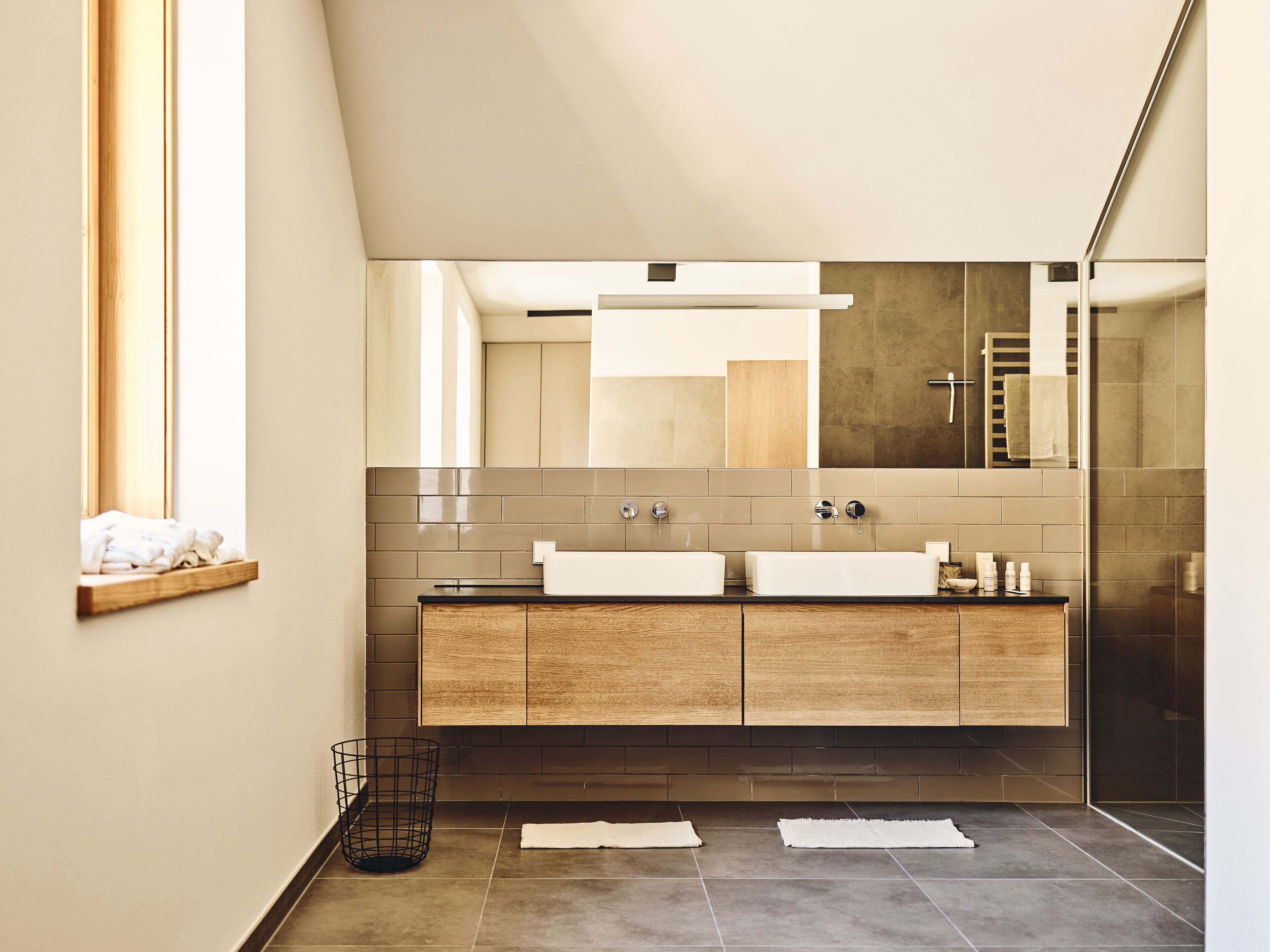 A modern bathroom with a large mirror, two sinks, and a wooden vanity.