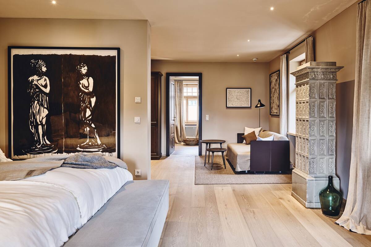 A hotel room with a large bed, a seating area with a sofa and a small table, a decorative cabinet, and a large painting on the wall.
