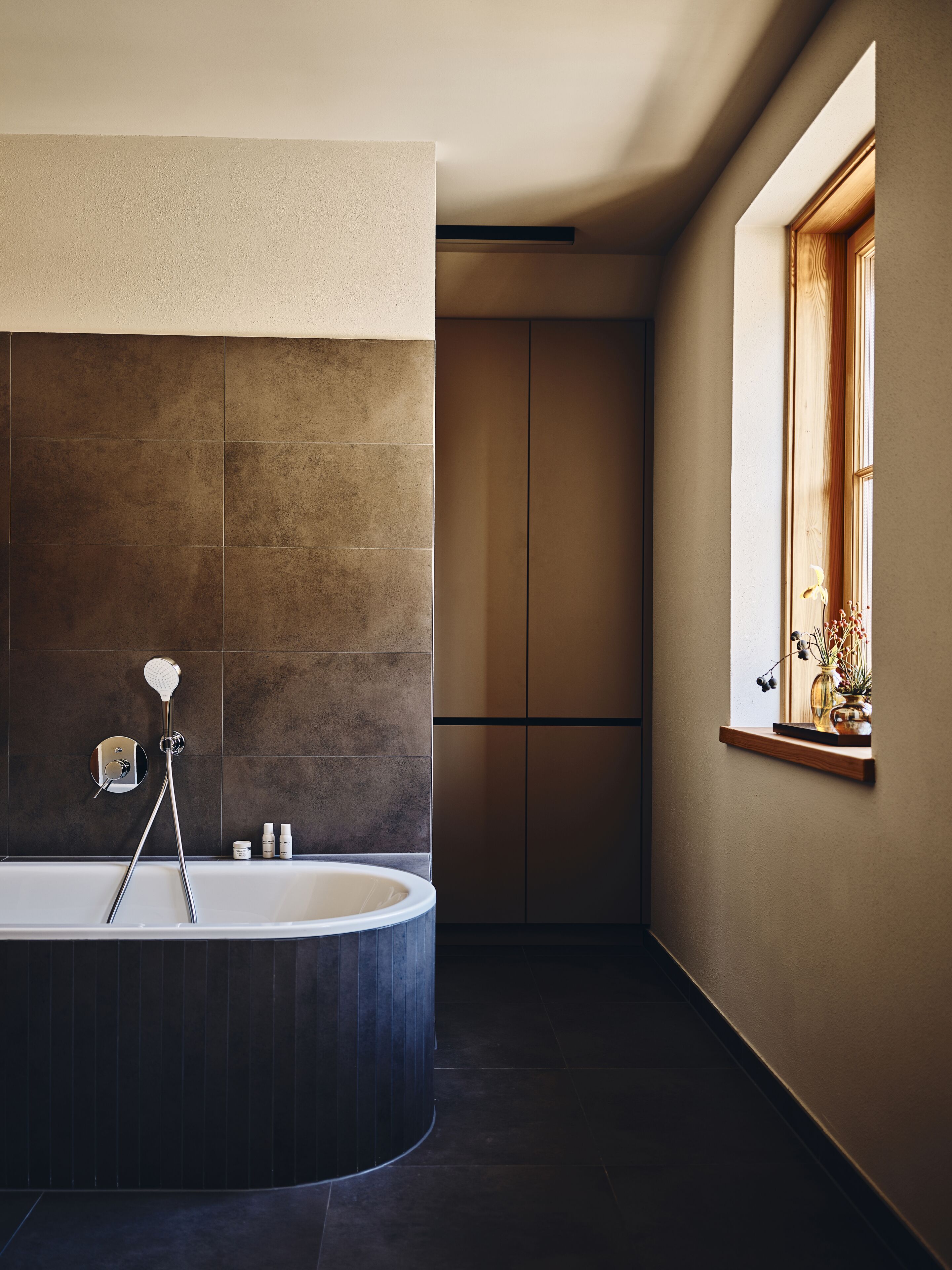 Une salle de bain moderne avec une baignoire sur pieds, une douche et une fenêtre donnant sur un jardin fleuri.