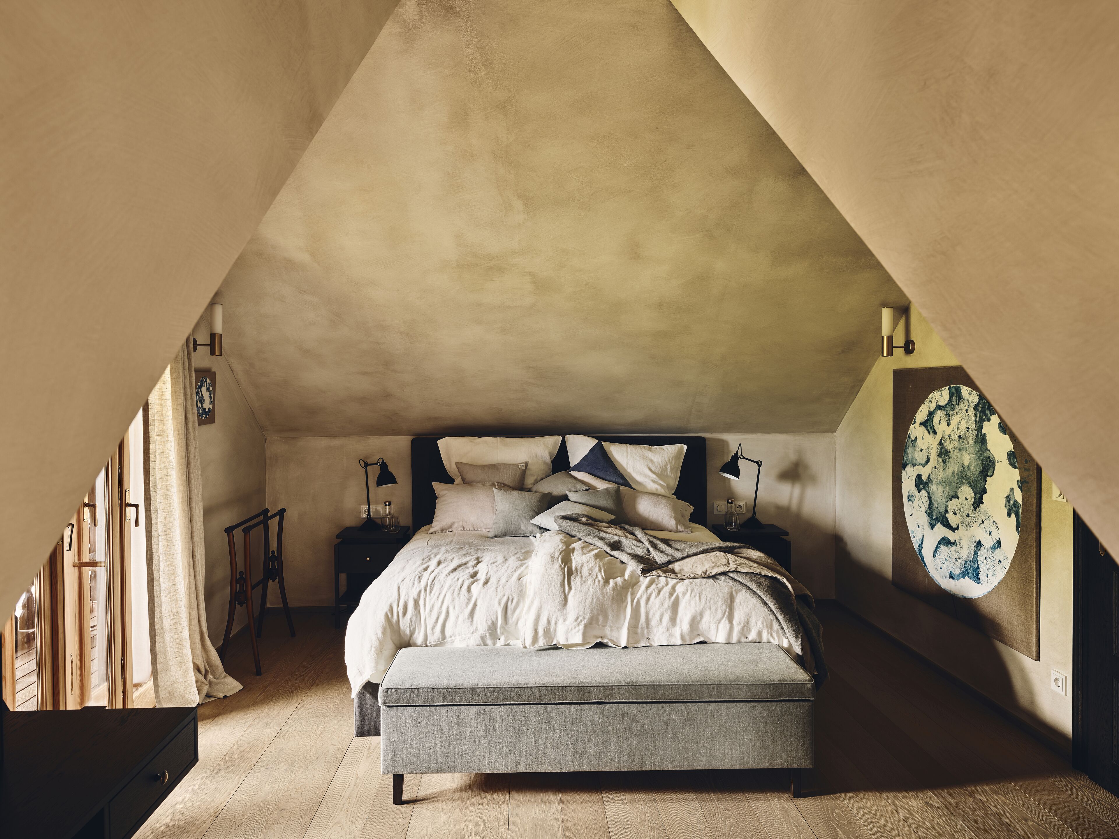 A bedroom with a sloped ceiling, a bed with multiple pillows, bedside lamps, and a wooden floor.