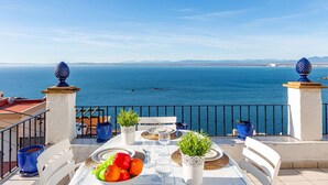 A terrace with a table set for dining, overlooking a coastal view with the sea and distant mountains. - Beautiful apartment in villa for 4 guests with pool, WIFI, TV and terrace (Roses)
