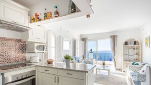 A modern kitchen with white cabinets, a microwave, and a stove. There is a dining area with a table and chairs, and a view of the sea through large windows. - Beautiful apartment in villa for 4 guests with pool, WIFI, TV and terrace (Roses)