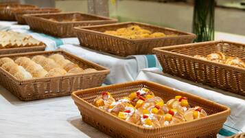A buffet table with various food items in wicker baskets, including bread rolls and pastries with fruit toppings.