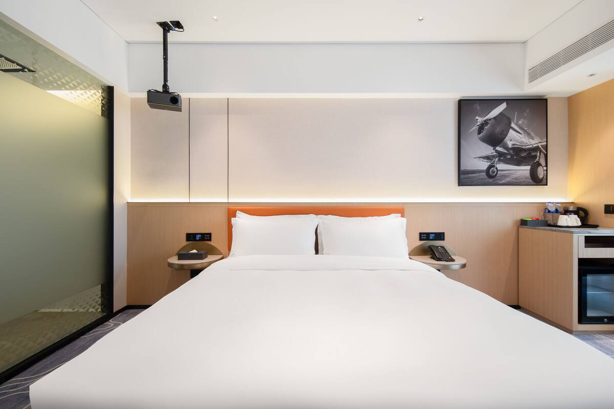 A hotel room with a large bed, a nightstand with a phone, a coffee machine, and a framed picture on the wall.