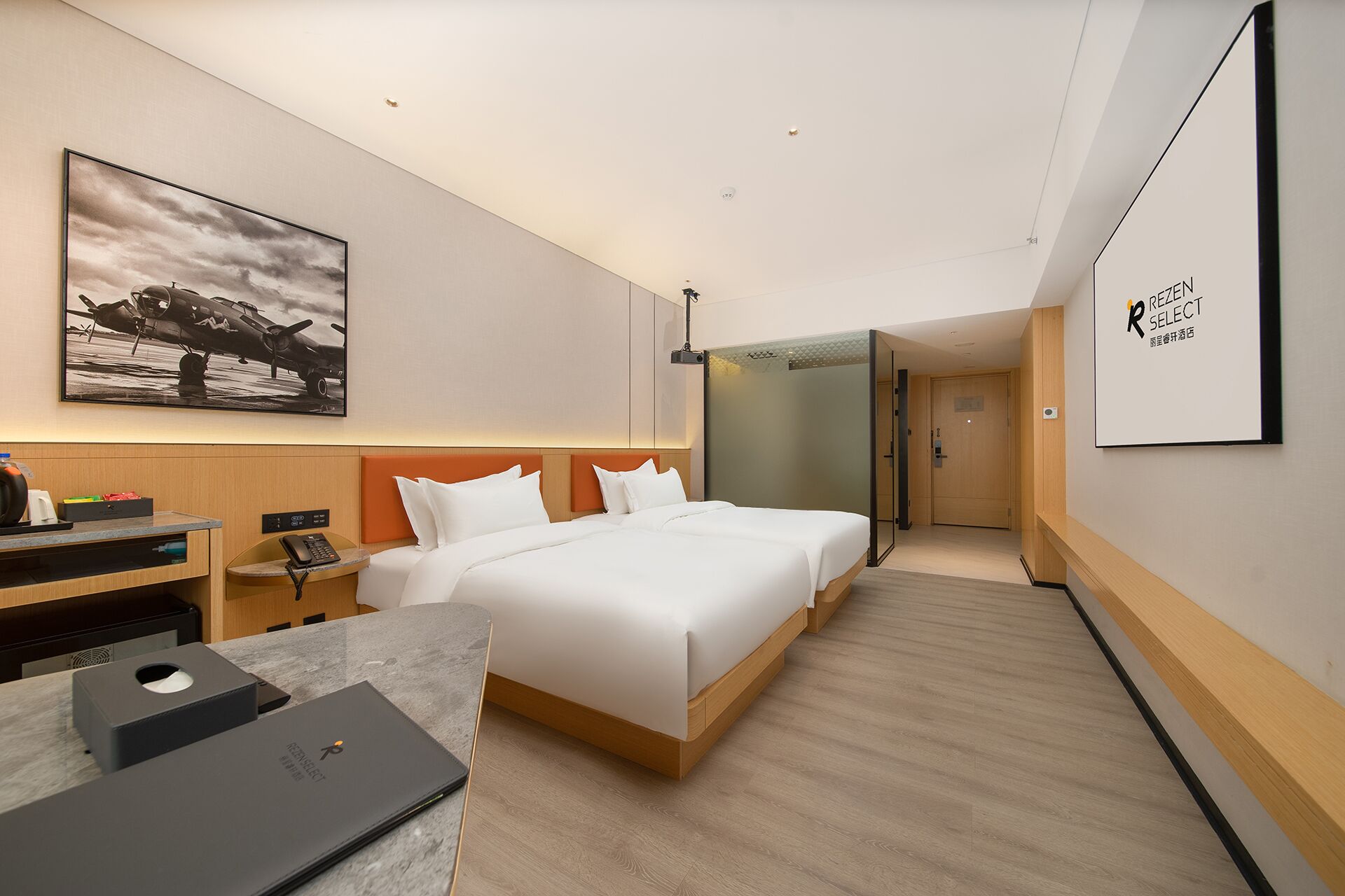 A hotel room with a bed, a desk, a chair, a telephone, a projector, and a framed picture on the wall.