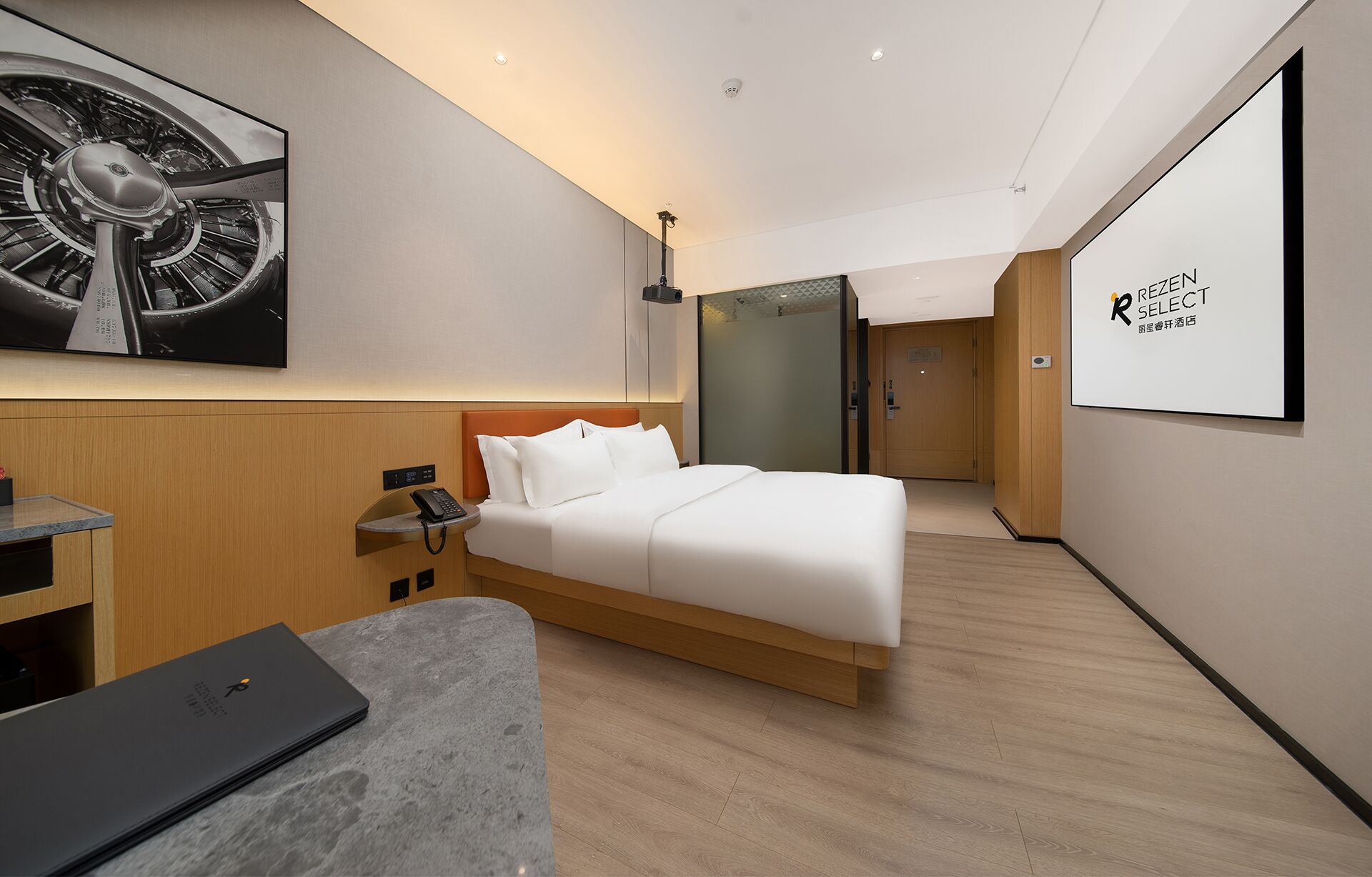 A modern hotel room with a bed, bedside table, and a desk with a laptop.