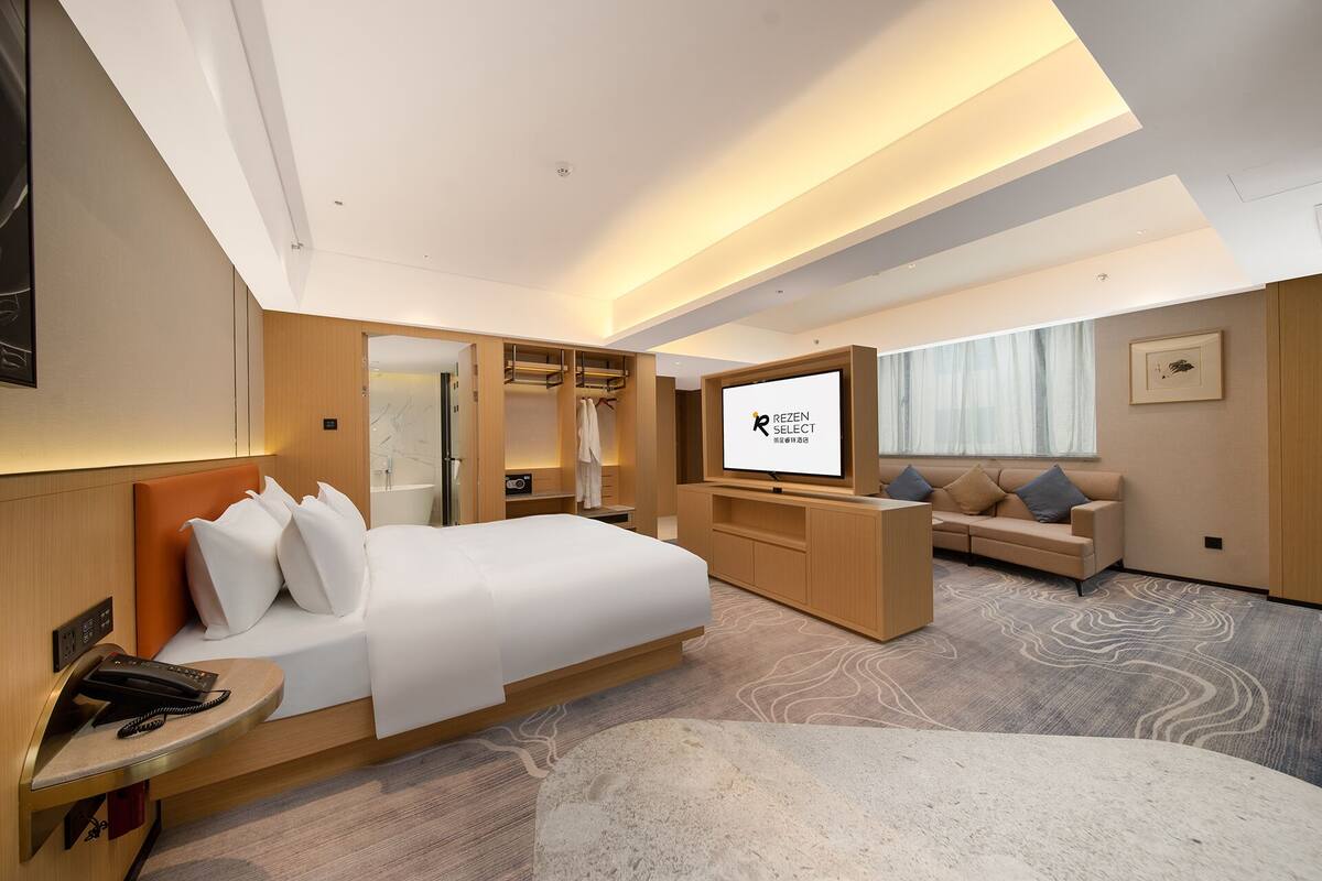 A modern hotel room with a large bed, a TV, a sofa, and a desk with a phone.