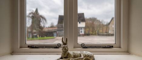 A window with a sculpture of a reclining animal on the sill, overlooking a residential street with houses and trees.