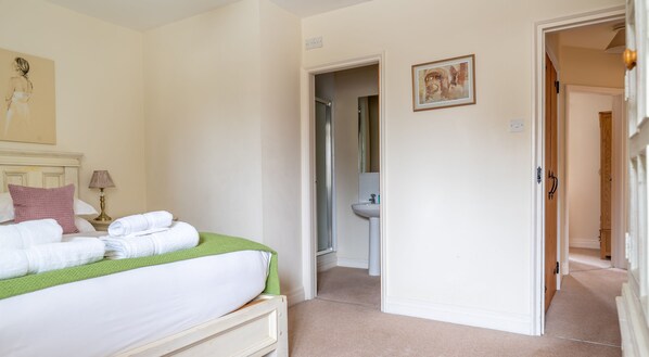 A hotel room with a bed, a green throw, white towels, a nightstand, a lamp, a painting, and a bathroom visible through an open door. - Crabtree - sleeps 4 guests in 2 bedrooms (Graythwaite)