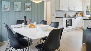 Eine moderne Küche mit weißen Schränken, einem eingebauten Backofen und einem Essbereich mit einem weißen Tisch und schwarzen Stühlen.