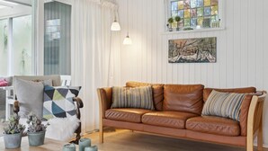 Ein Wohnzimmer mit einer braunen Ledersofa, zwei Kissen, einem weißen Sessel, einem Holztisch und einer kleinen Topfpflanze.
