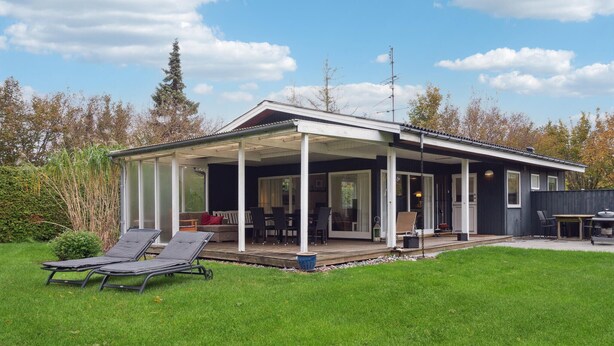 Ein modernes Haus mit überdachter Terrasse, Rasenfläche und Garten.