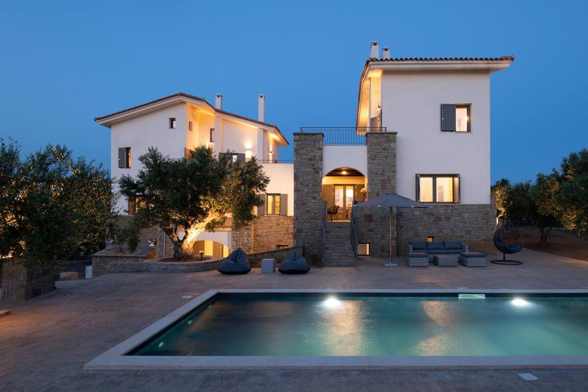A modern two-story house with a swimming pool, stone pillars, and outdoor seating.