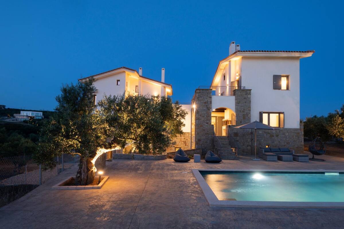 A modern villa with a swimming pool, stone architecture, and outdoor seating.