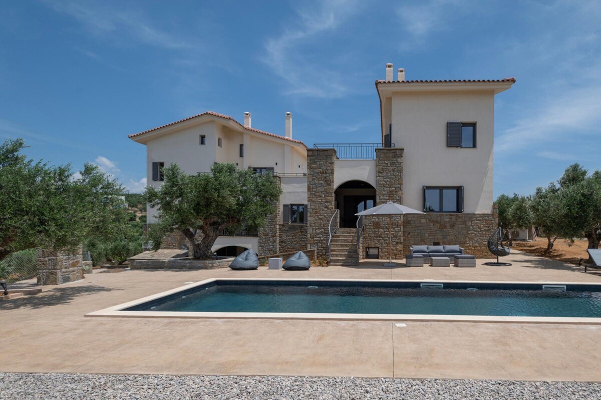A two-story house with a swimming pool, stone walls, and outdoor seating.