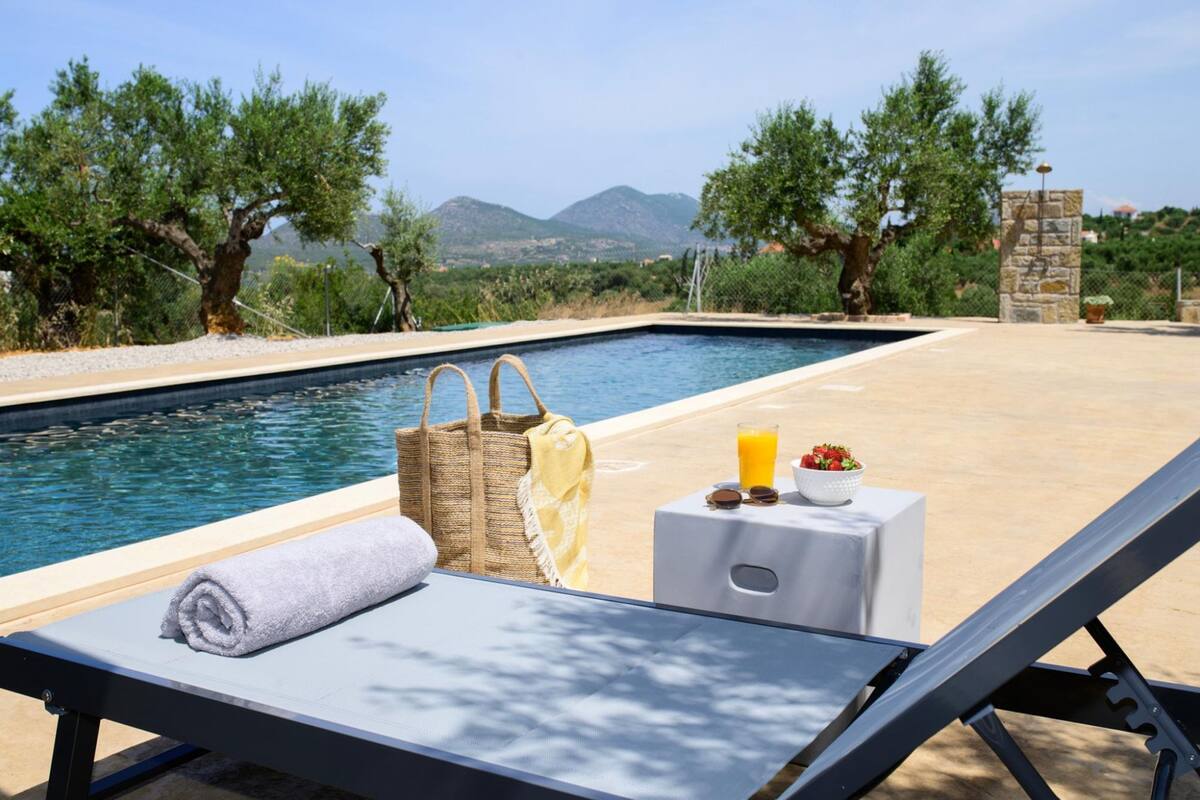 A poolside area with a lounge chair, a towel, a basket, and a table with a drink and a bowl of fruit.