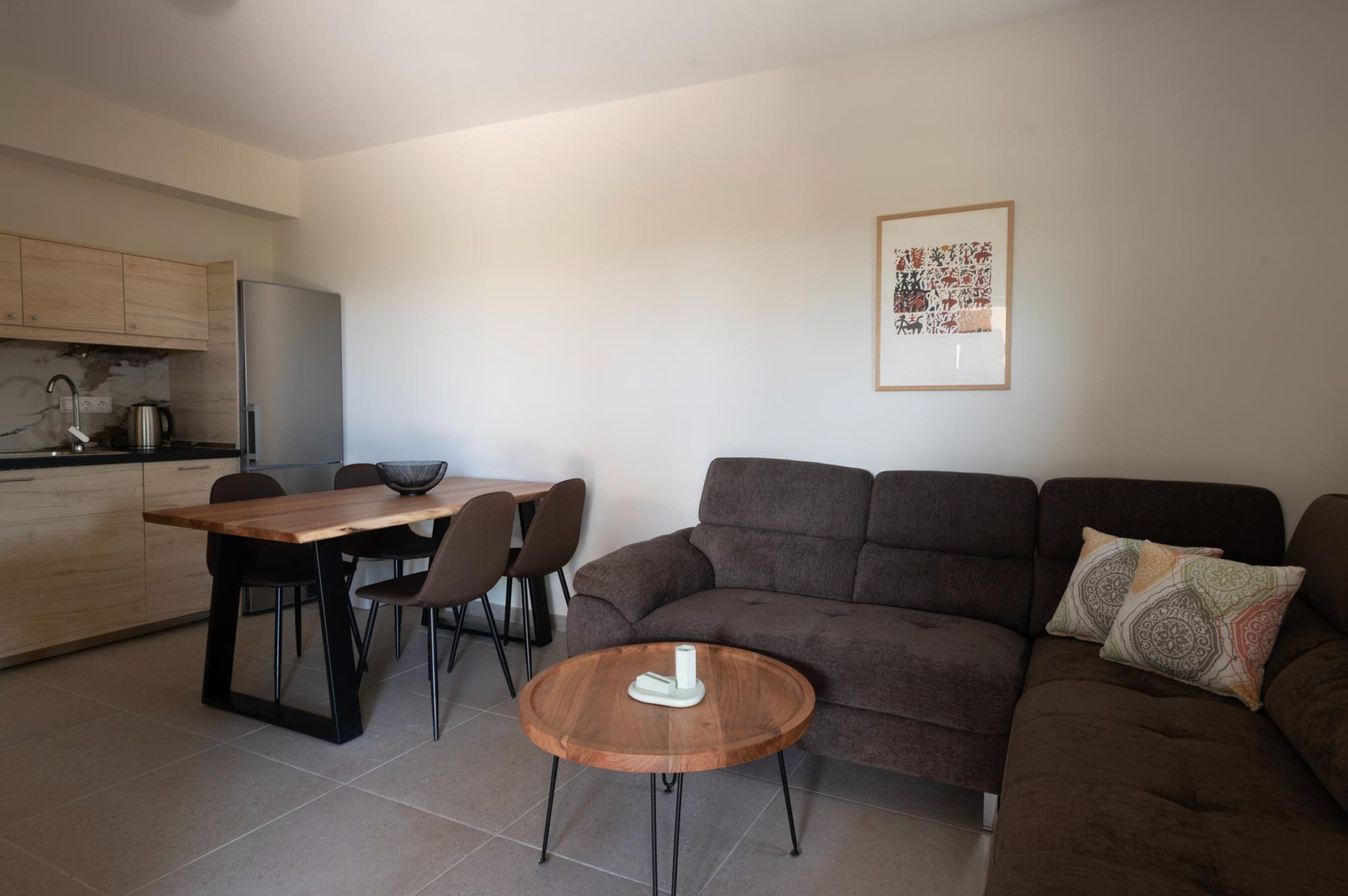 A modern living room with a brown sofa, a wooden coffee table, and a dining area with a wooden table and chairs.