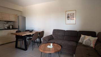 A modern living room with a brown sofa, a wooden coffee table, and a dining area with a wooden table and chairs.
