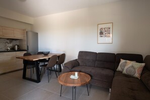 A modern living room with a brown sofa, a wooden coffee table, and a dining area with a wooden table and chairs. - Modone Villas in Peloponnese (Pylos-Nestoras)