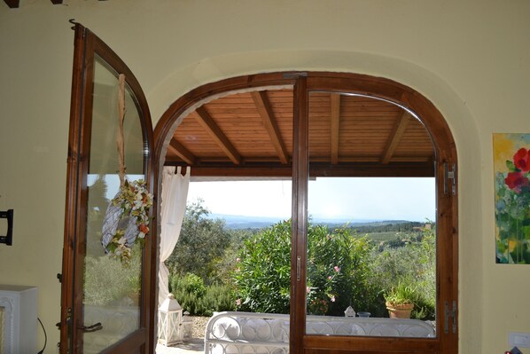 A room with a wooden ceiling, a view of a landscape with trees and hills, and a potted plant on a balcony.