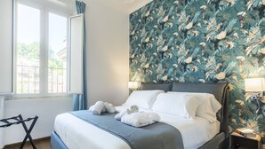 Un lit bien fait, avec du linge de lit blanc, une tête de lit bleue et un papier peint orné de motifs de feuilles tropicales.