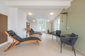 A sunlit room with three sun loungers, a wicker chair, and a large window. - Hochwertiges Appartement in Ruhiger Lage, mit Stellplatz (Zirchow)