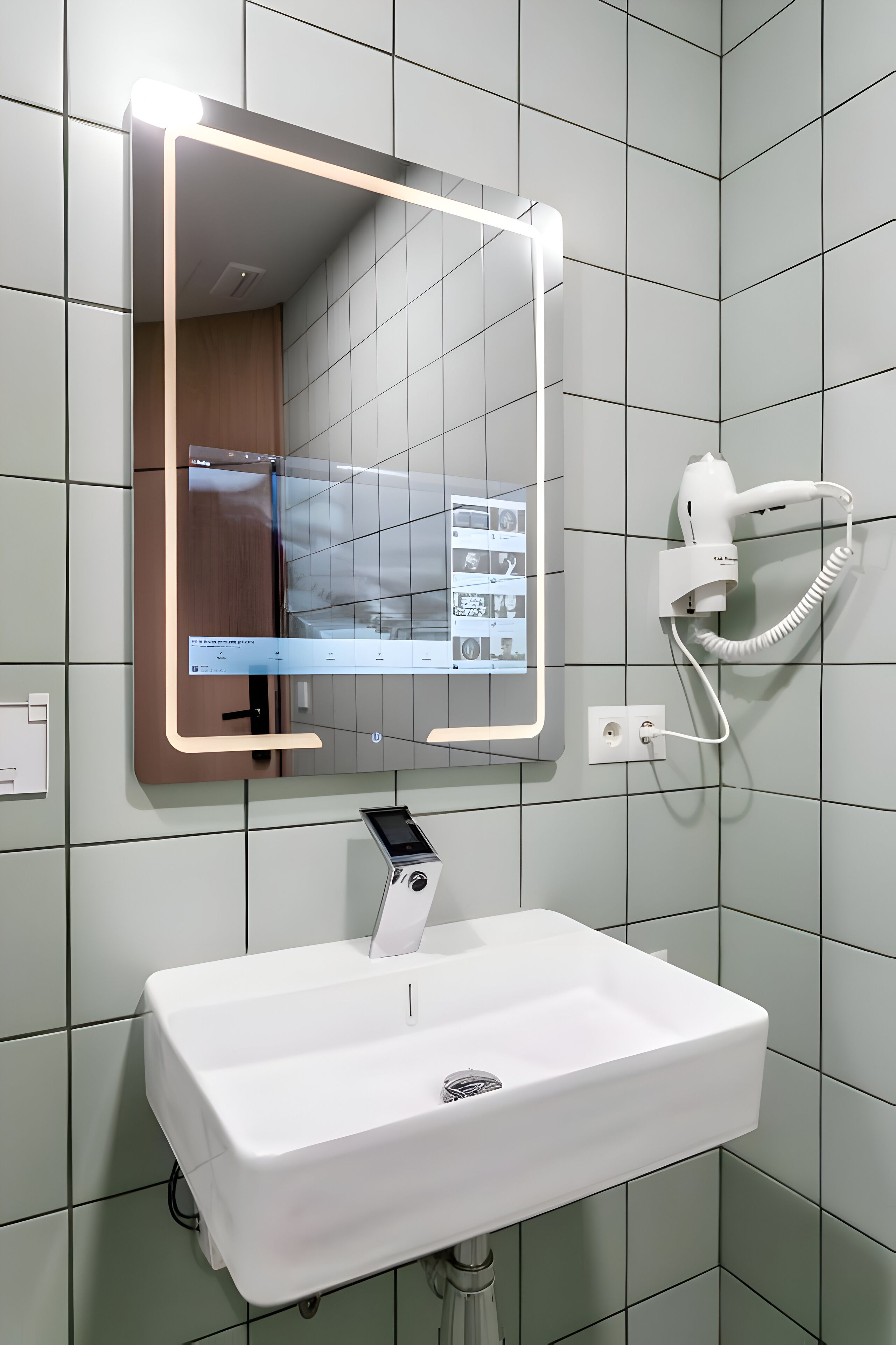 Ein Badezimmer mit einem weißen Waschbecken, einem Spiegel mit beleuchtetem Rand und einem an der Wand befestigten Föhn.