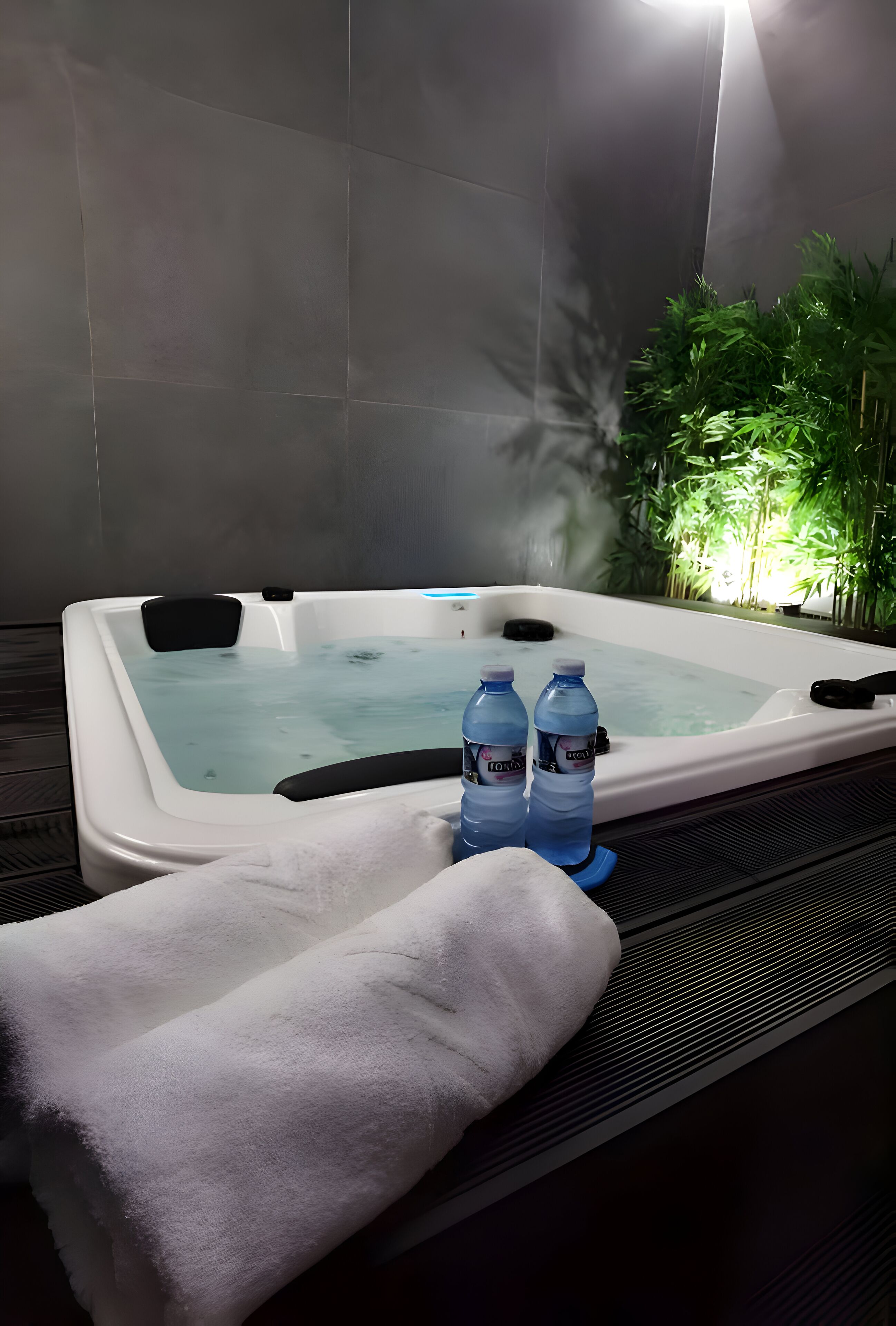Un jacuzzi con dos botellas de agua, una toalla y una planta al fondo.