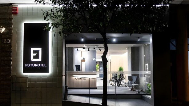 Entrada de un hotel FUTUROTEL de diseño moderno, que incluye un mostrador de recepción, una zona de estar y una bicicleta estacionada afuera.