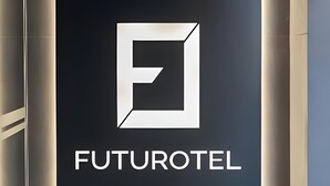 Letrero de FUTUROTEL con un logotipo geométrico y el nombre en blanco sobre fondo oscuro, flanqueado por macetas con plantas y piedras blancas.