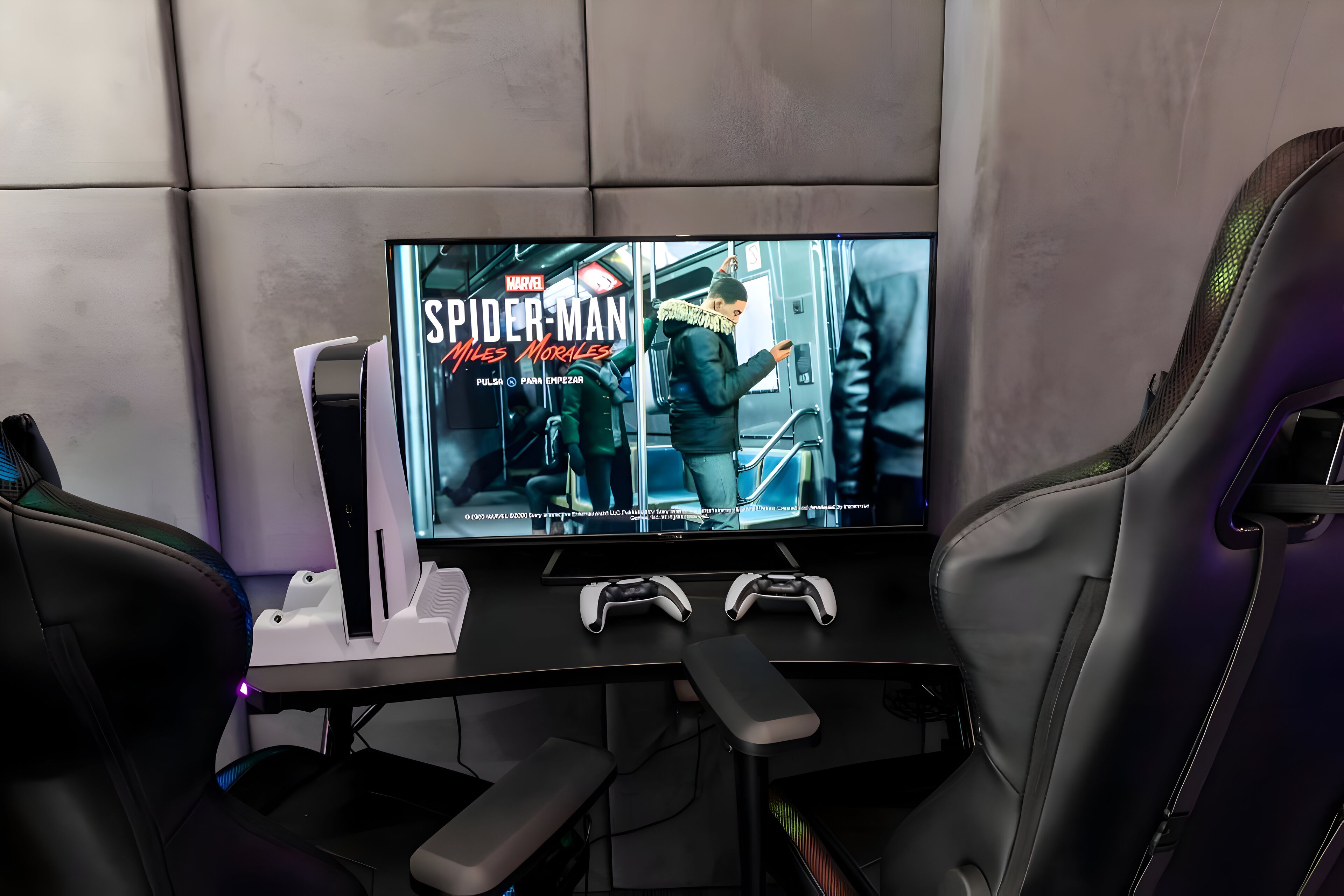 Een game-opstelling met een groot beeldscherm, twee gamecontrollers en een stoel.
