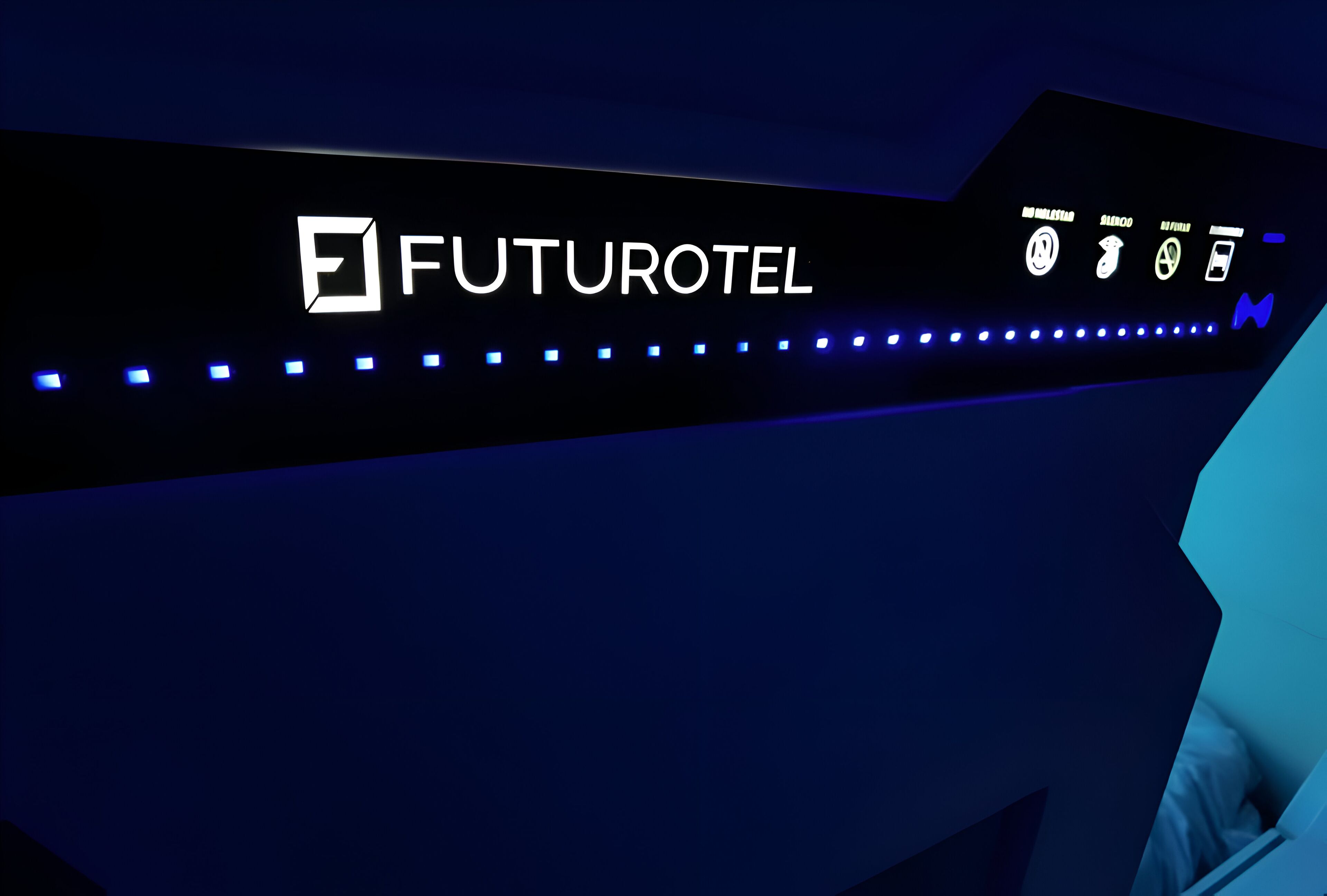 Un cartell futurista d'hotel amb el nom FUTUROTEL, i icones que representen serveis com ara un lavabo, un llit i un telèfon mòbil.