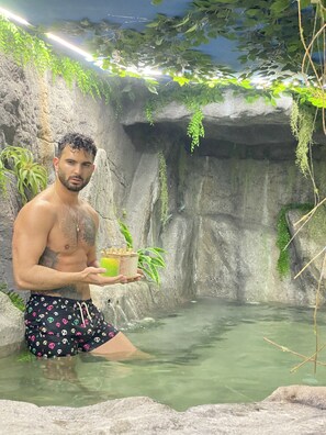 A man in a natural setting with a pool, holding a drink, surrounded by greenery and rocks. - Futurotel Spa Garden (Granada)