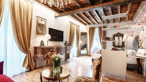 A room with a wooden ceiling, a TV, a dining table with chairs, a sofa, and a bookshelf. - Aurum - Como Luxury Suites (Como)
