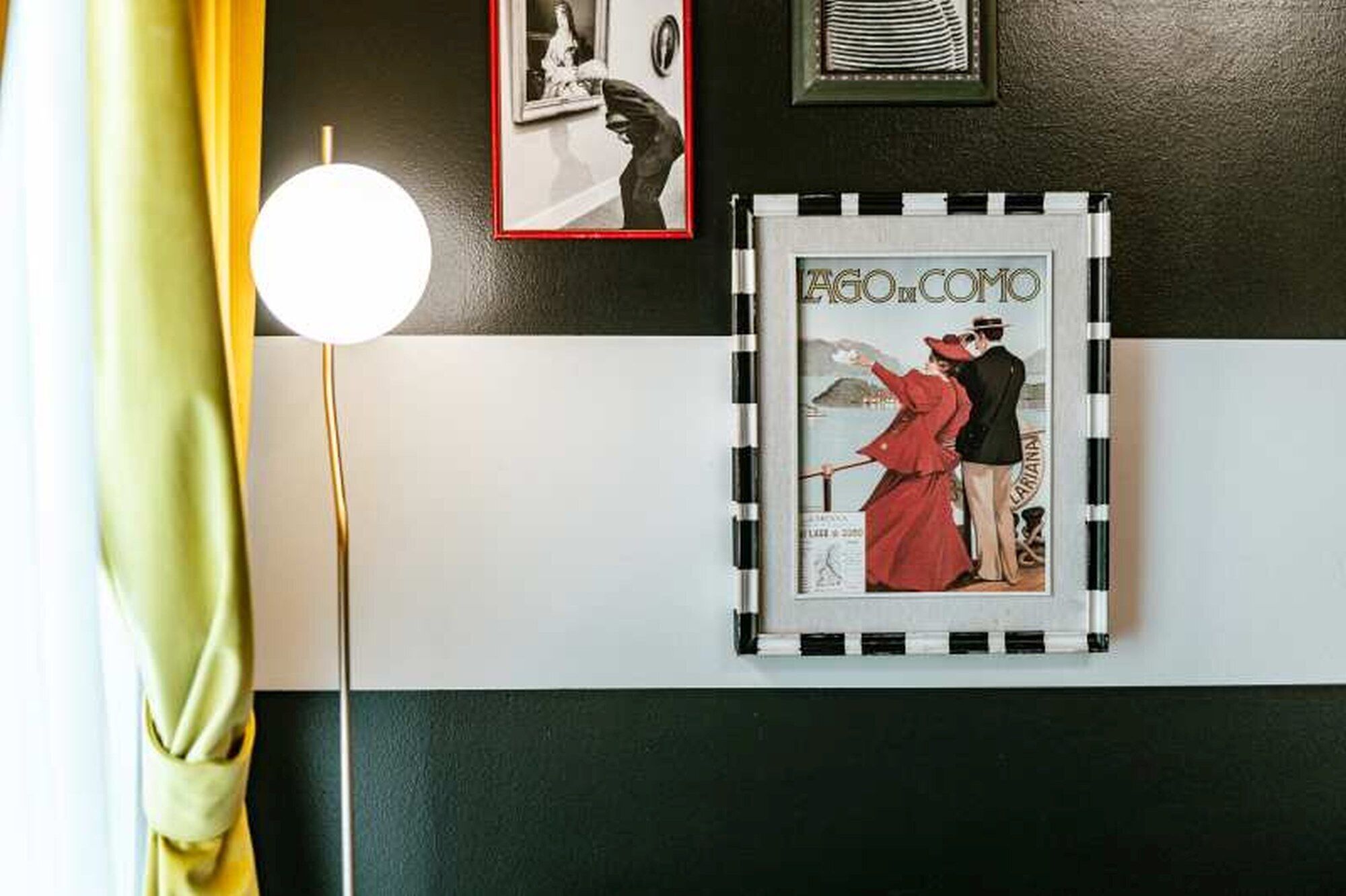 Eine Wand mit schwarz-weiß gestreiftem Muster, ein gerahmter Vintage-Poster und eine Stehlampe.
