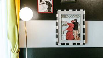 Eine Wand mit schwarz-weiß gestreiftem Muster, ein gerahmter Vintage-Poster und eine Stehlampe.