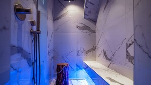 A modern bathroom with marble walls, a built-in shower, and a blue-lit tub. - Aurum - Como Luxury Suites (Como)