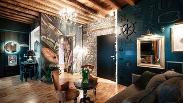 A cozy room with a wooden ceiling, a chandelier, a dining table with chairs, a sofa, and a wall with decorative elements.