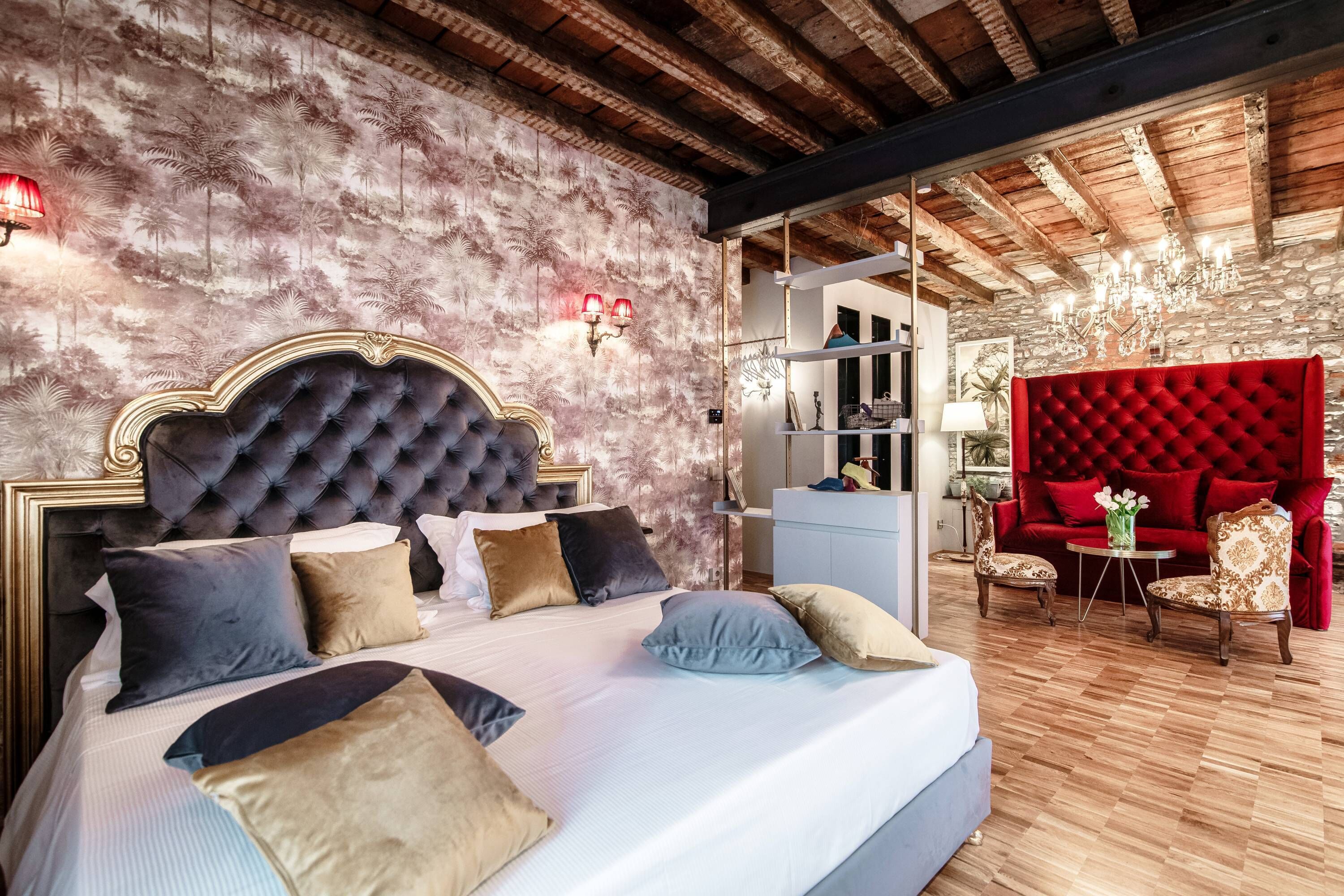 Une chambre avec un grand lit, un canapé rouge recouvert de tissu et un mur en pierre.