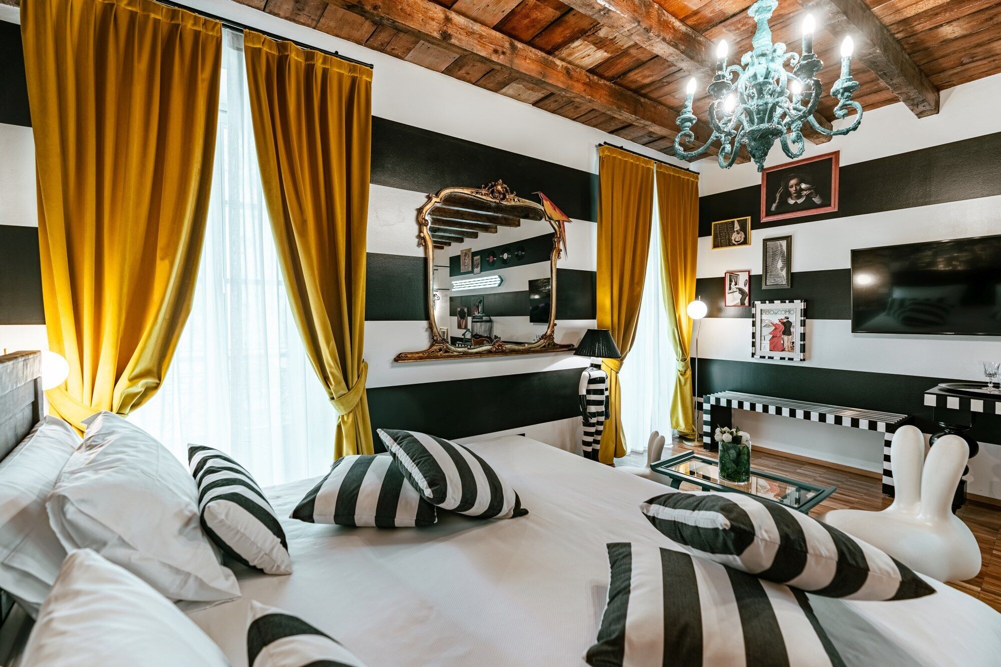 A hotel room with a bed, a vanity with a mirror, a chandelier, and a television on the wall.
