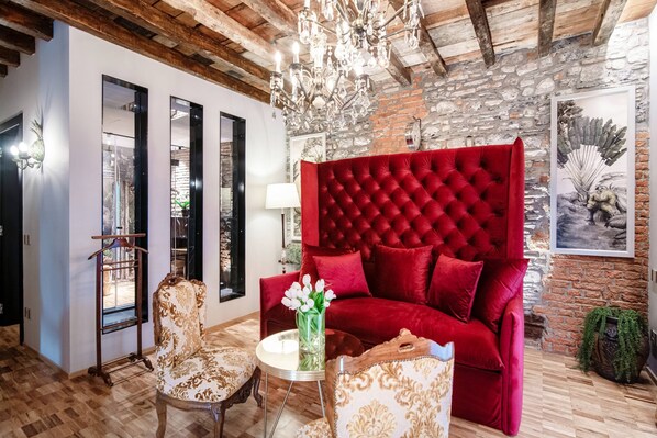 A room with a red velvet sofa, a chandelier, and a wooden ceiling.