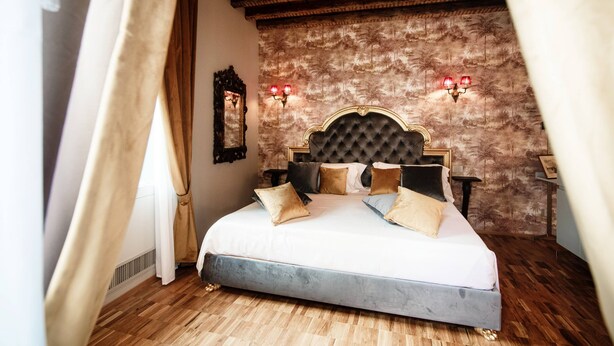 A bedroom with a large bed, wooden ceiling beams, a patterned wall, and two wall-mounted lamps. - Aurum - Como Luxury Suites (Como)
