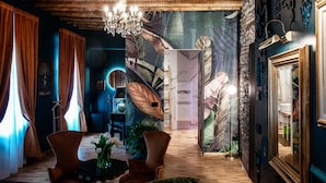 A cozy room with a wooden ceiling, a chandelier, a large leaf mural, and a mirror. - Aurum - Como Luxury Suites (Como)