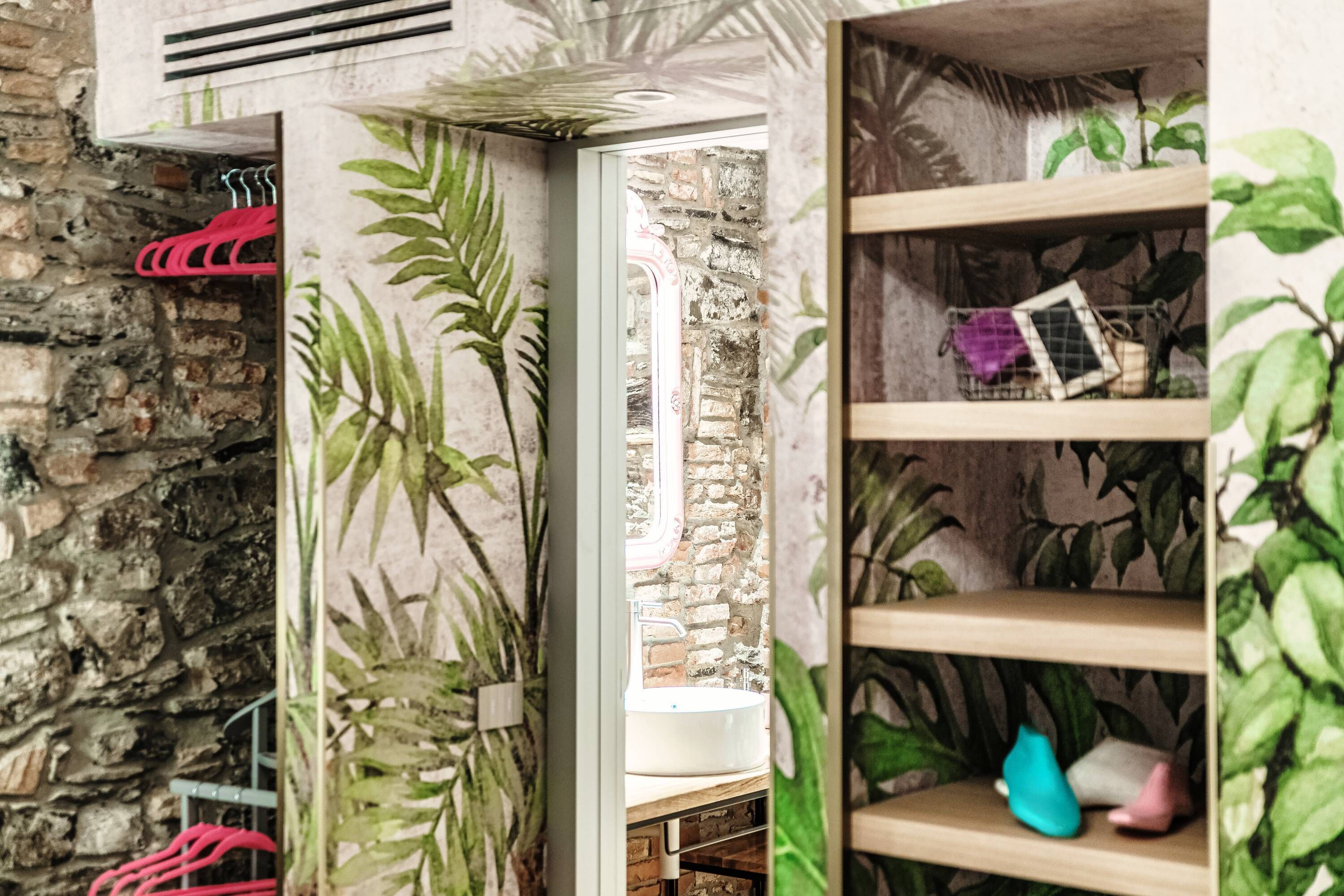 Un baño con pared de piedra, un lavabo blanco y estantes con plantas y una jaula pequeña.