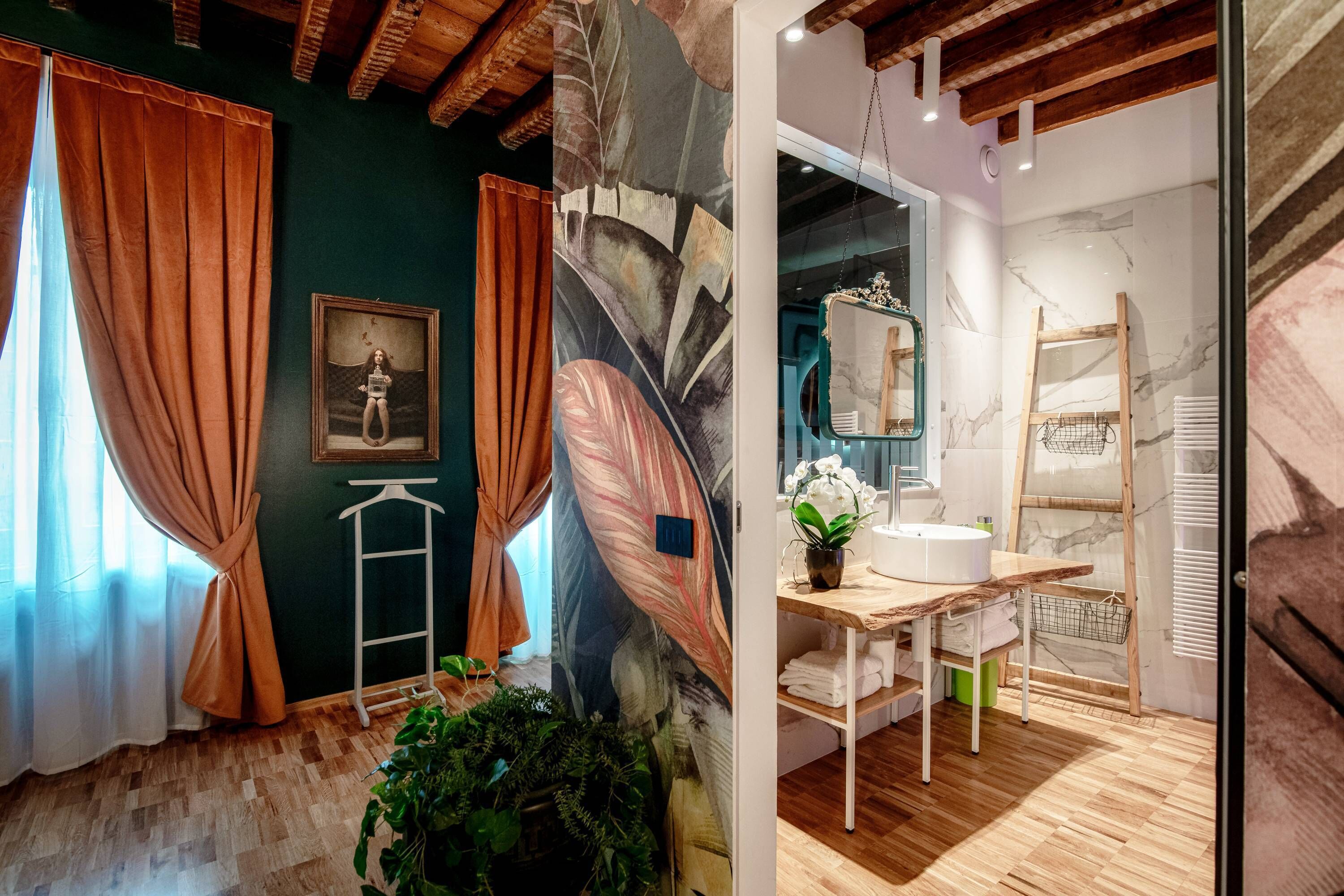 A room with a wooden floor, a large abstract painting, a framed picture, and a window with orange curtains.
