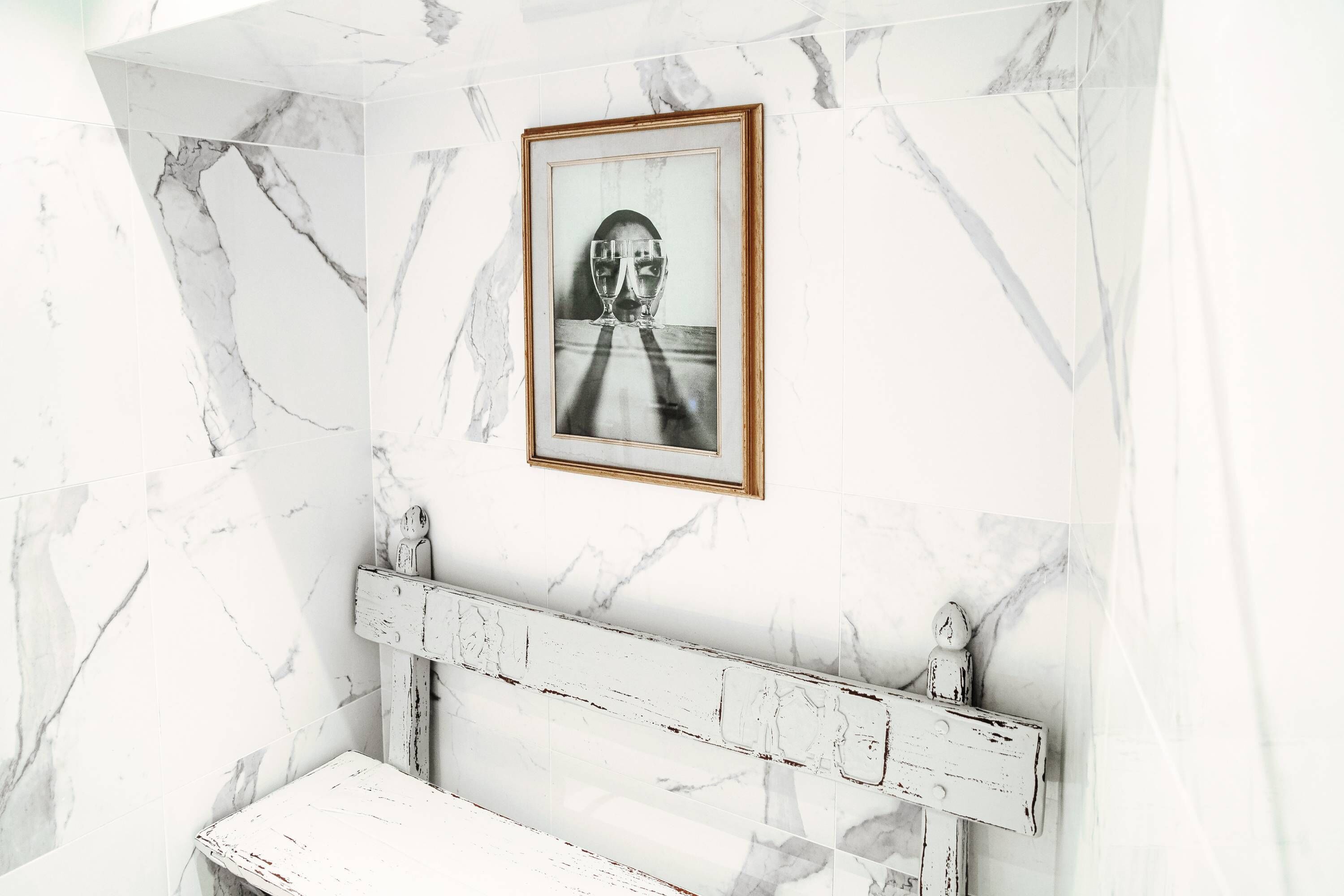Une salle de bain aux murs recouverts de marbre, ornée d’un tableau encadré et comprenant un banc rustique.
