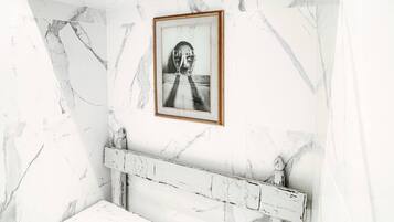 Une salle de bain aux murs recouverts de marbre, ornée d’un tableau encadré et comprenant un banc rustique.