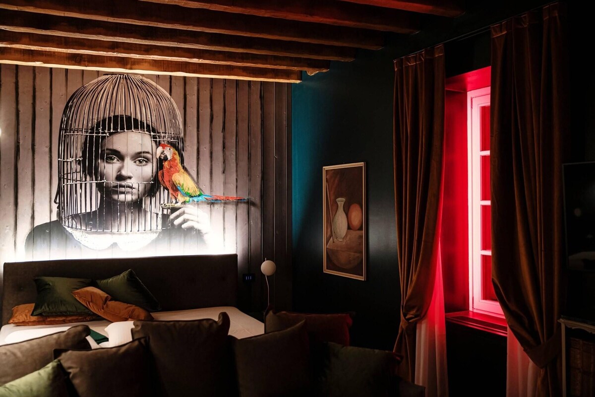 A room with a bed, a wall with a large mural, a window with red curtains, and a wooden ceiling.
